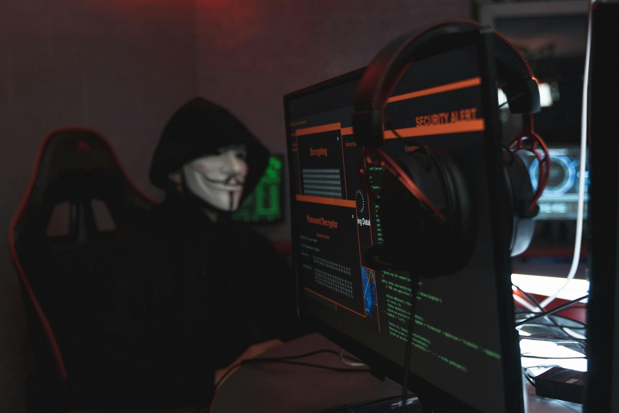 person wearing a mask sitting at a desk monitoring security systems
on a computer screen